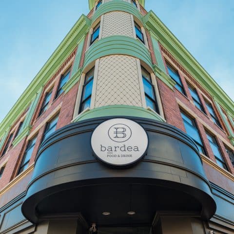 Exterior of tall art-deco building with green trim and a Bardea Food & Drink sign