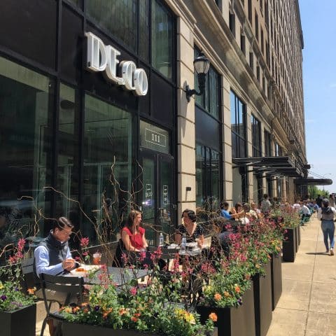 City street on a sunny day showing exterior of Deco with outdoor tables and chairs