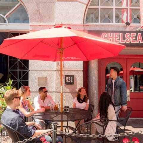 Group of friends sitting at outdoor table under umbrella outside of Chelsea Tavern
