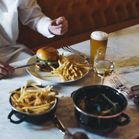 Restaurant table with full wine glass and beer glass and a plate of burger and fries